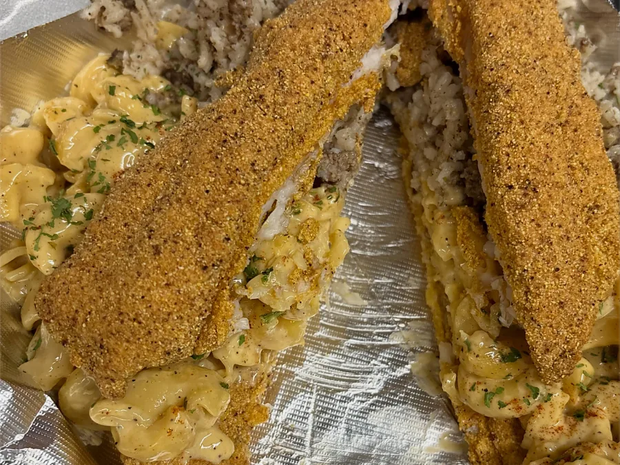 Two cornmeal-crusted catfish fillets stuffed with mac and cheese and dirty rice, on foil in a takeout box