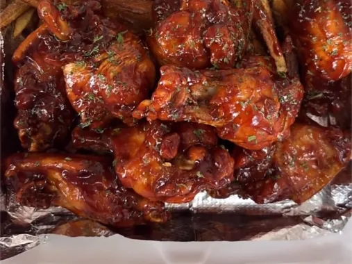 Glazed red-sauced chicken wings piled over fries in a takeout box