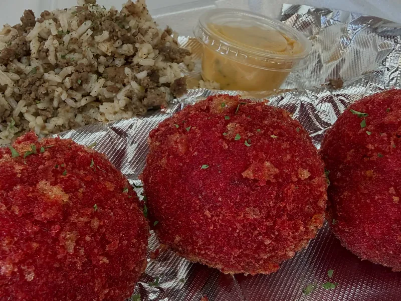 Three red-crusted fried boudin balls on foil, with dirty rice and a cup of dipping sauce