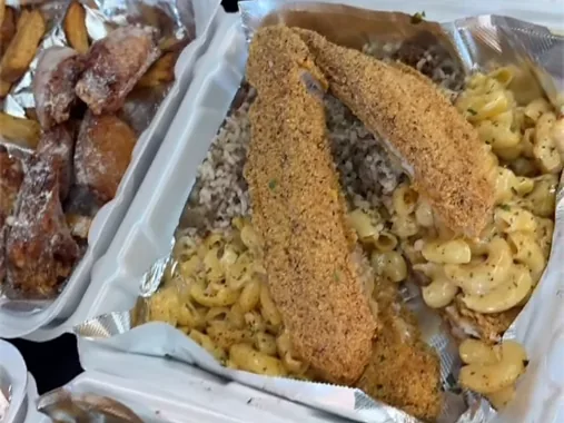 Open takeout boxes: crusted fish fillets over mac and cheese, next to a box of wings and fries