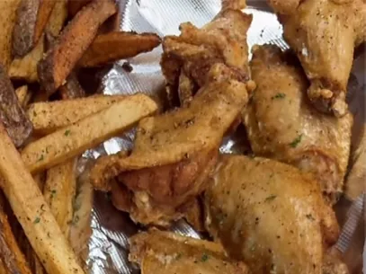 Fried chicken wings next to thick-cut fries on foil