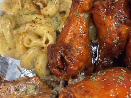 Glazed chicken wings next to a pile of mac and cheese on foil